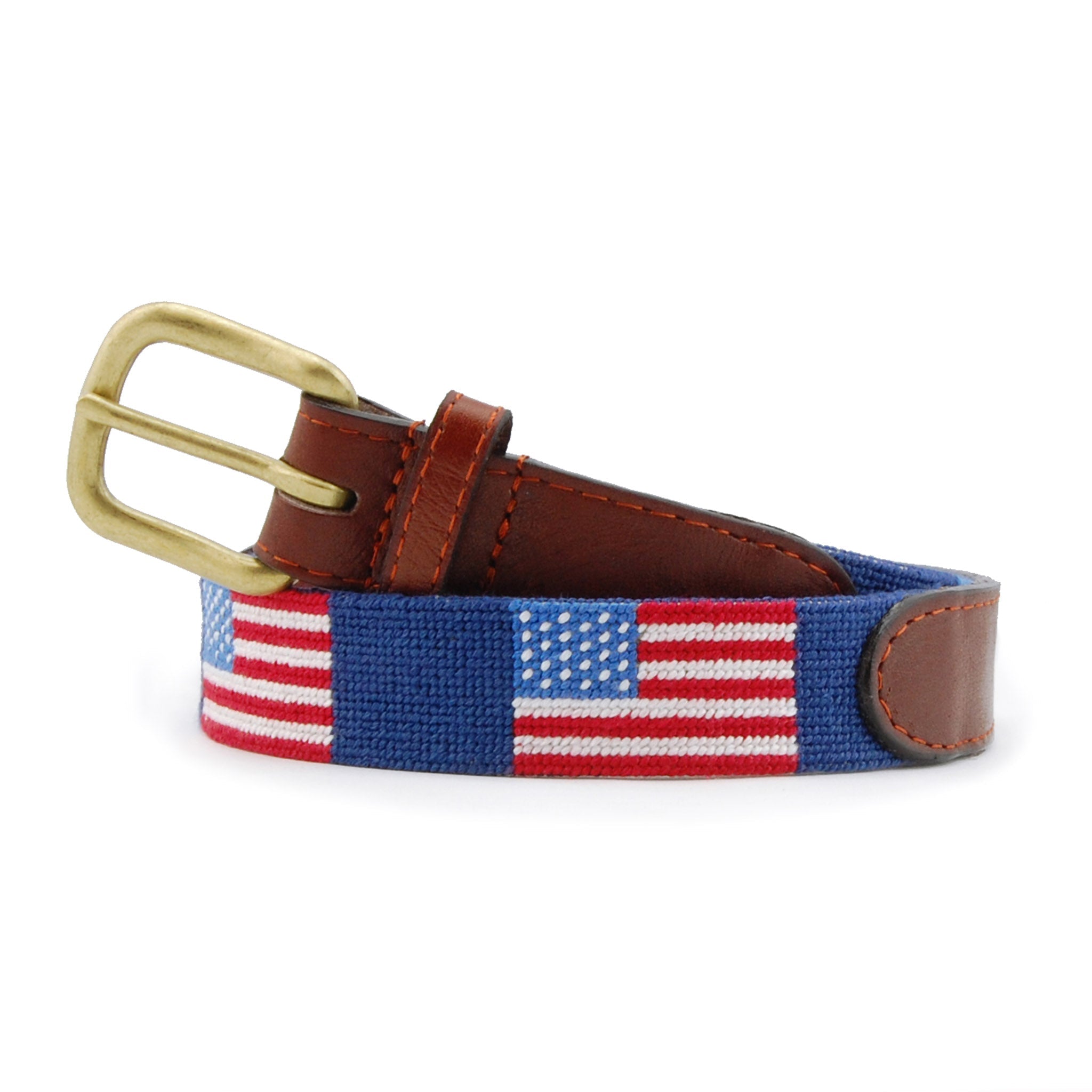 Children’s belt coiled with the stitched American flag design on a classic navy needlepoint background, finished with brown leather and a brass buckle.