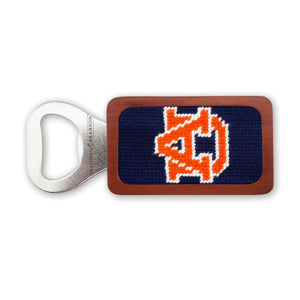 A stainless steel bottle opener with a wooden frame featuring a dark navy needlepoint design embroidered with the Auburn University “AU” logo in orange and white