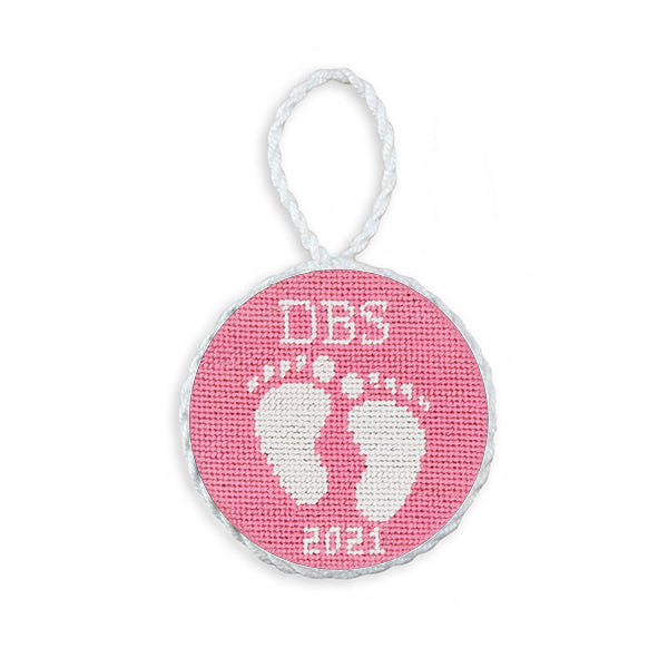 Pink needlepoint ornament featuring baby feet, finished with a white hanging cord.