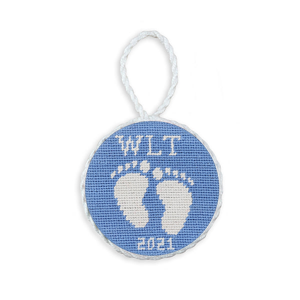 Light blue needlepoint ornament featuring baby feet, finished with a white hanging cord.