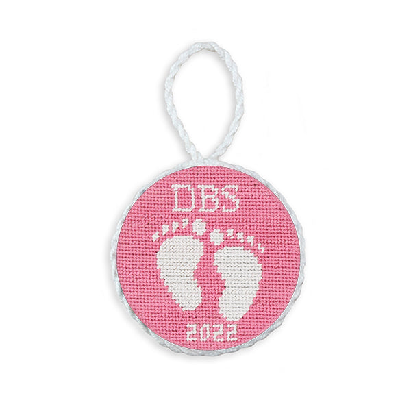 Pink needlepoint ornament featuring baby feet, white hanging cord, 2022 edition.