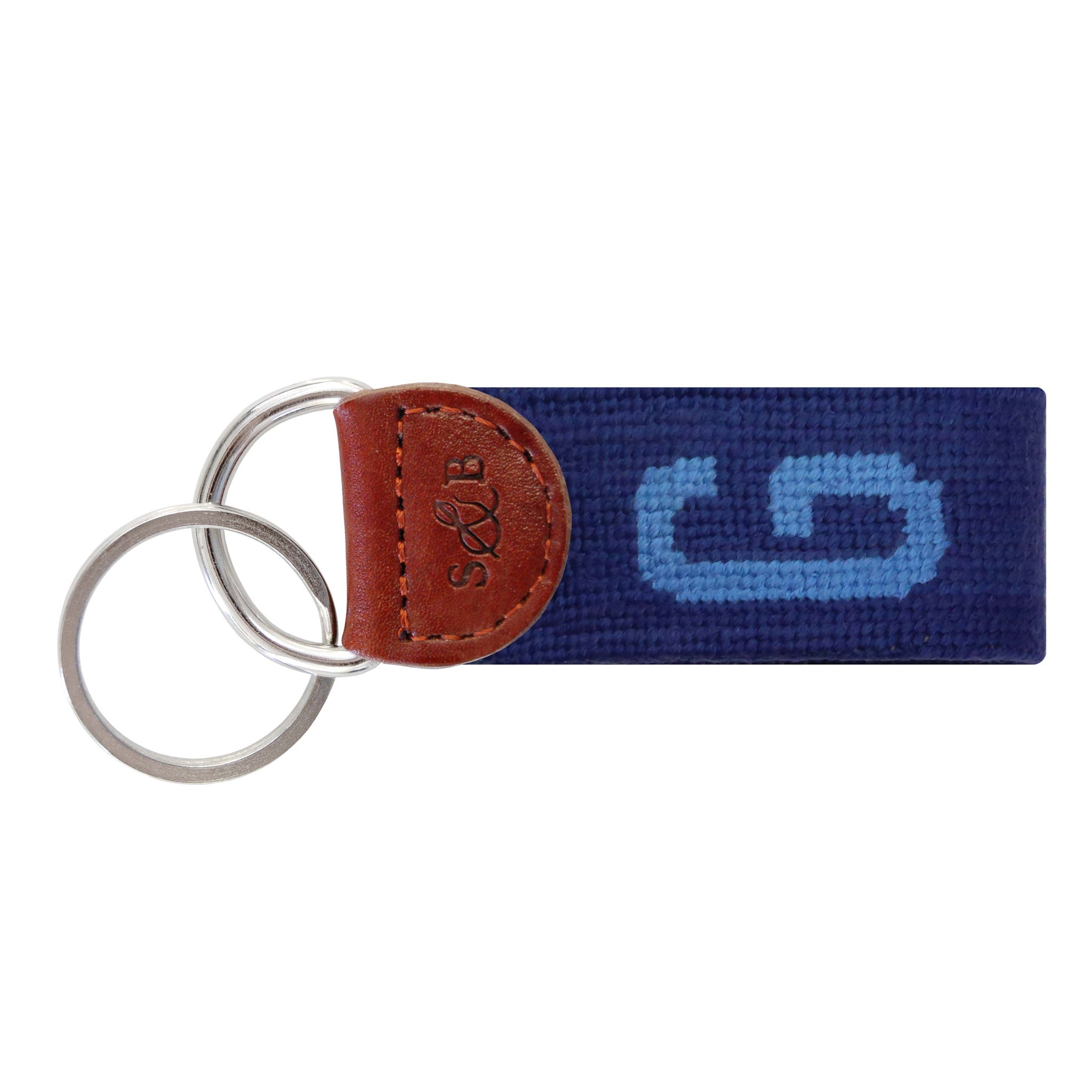 Navy needlepoint key fob with a white block letter “G,” brown leather trim, and a metal key ring.