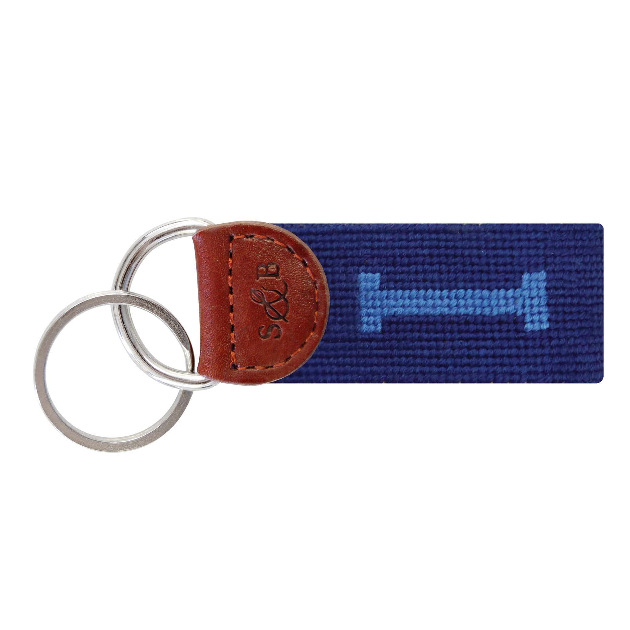 Navy needlepoint key fob displaying a white block letter “I,” brown leather trim, and a metal key ring.