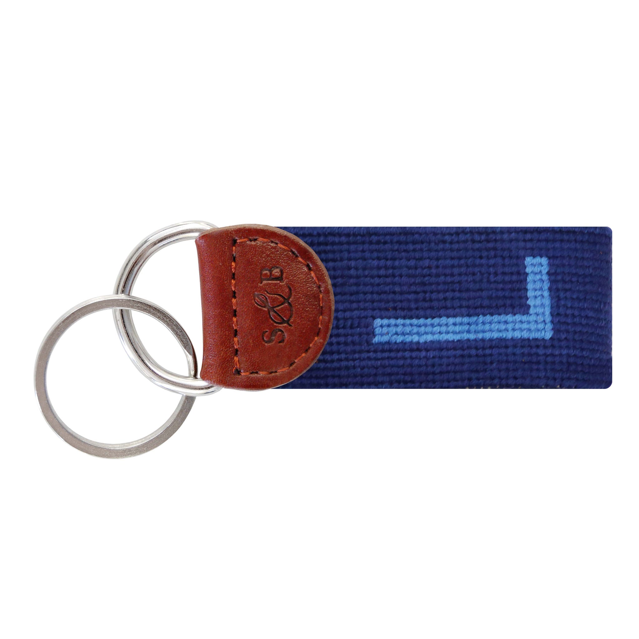 Navy needlepoint key fob displaying a white block letter “L,” brown leather trim, and a metal key ring.