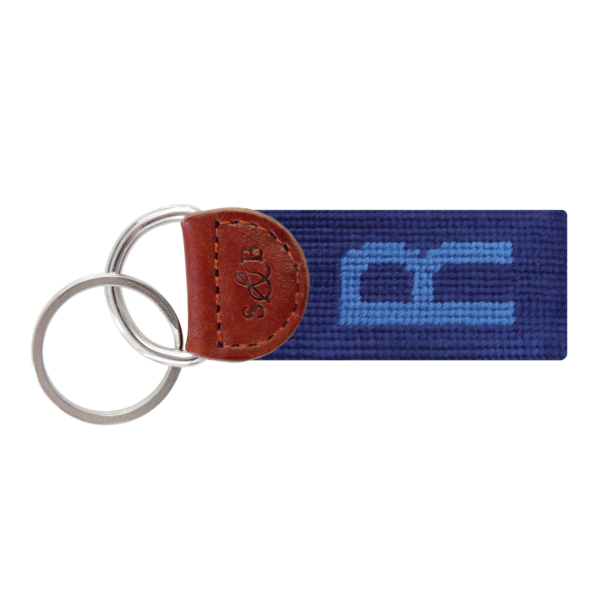 Navy needlepoint key fob displaying a white block letter “R,” brown leather trim, and a metal key ring.