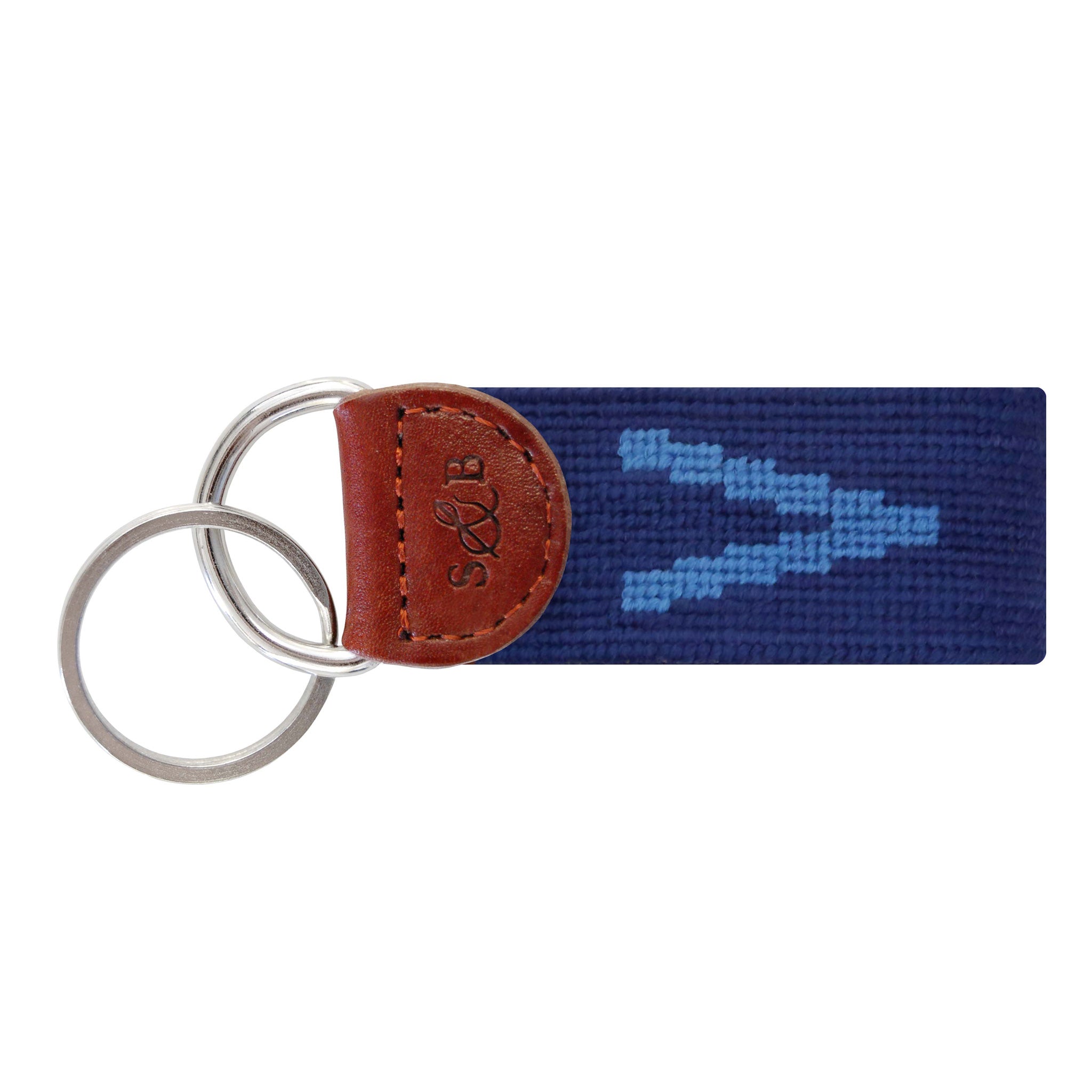 Navy needlepoint key fob displaying a white block letter “V,” brown leather trim, and a metal key ring.