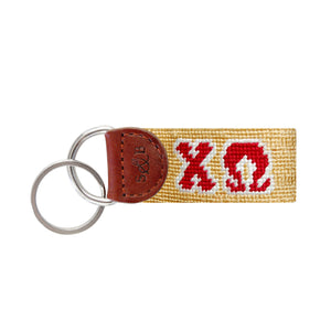 Red needlepoint key fob featuring the Greek letters ΧΩ in yellow, brown leather trim, and a metal key ring.