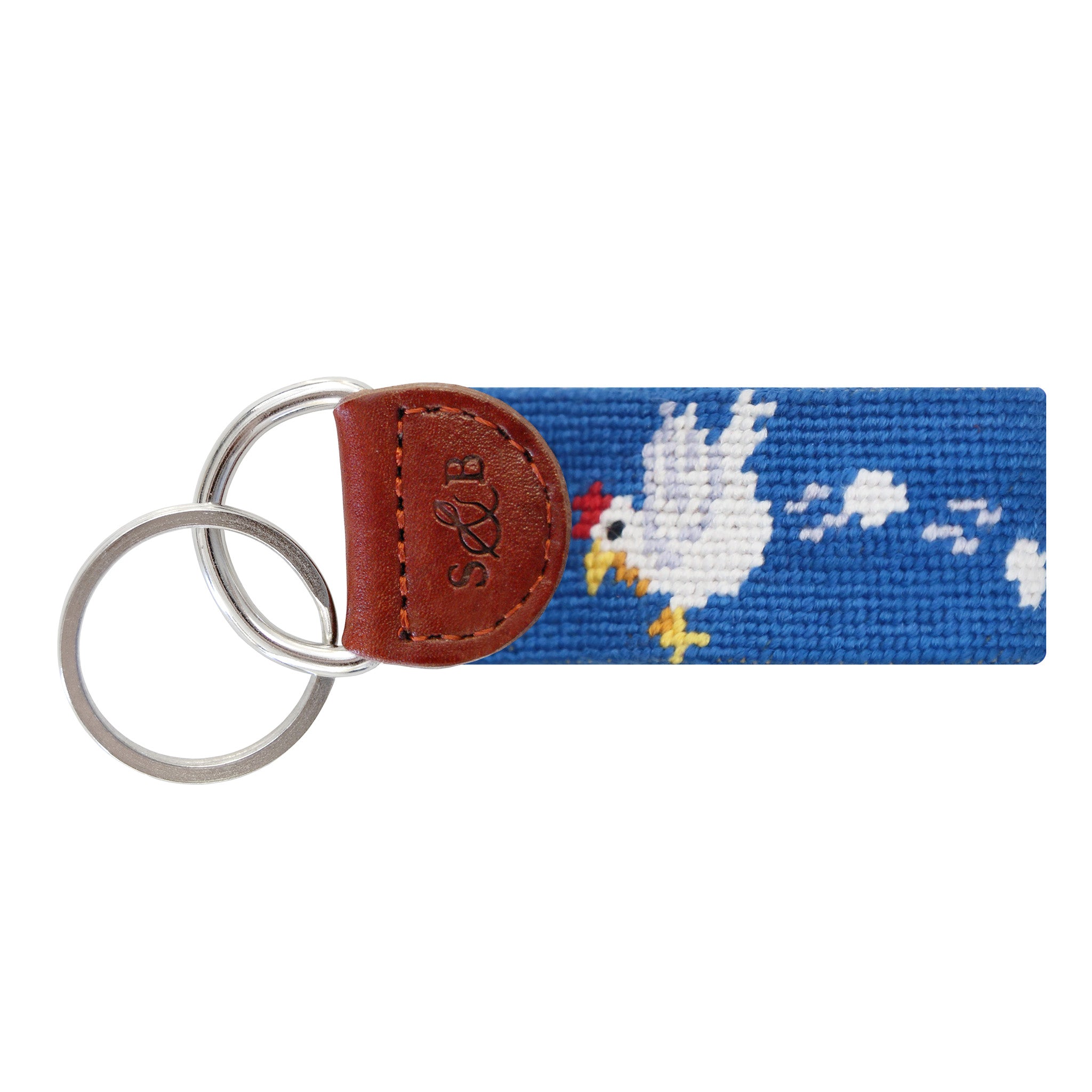 Blue needlepoint key fob with a fried egg and slice of ham motif, brown leather trim, and a metal key ring.