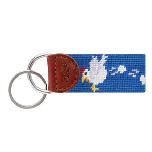Blue needlepoint key fob with a fried egg and slice of ham motif, brown leather trim, and a metal key ring.