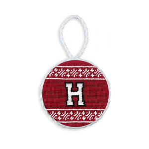 Garnet needlepoint ornament featuring the white Harvard “H” shield logo, finished with a white hanging cord.