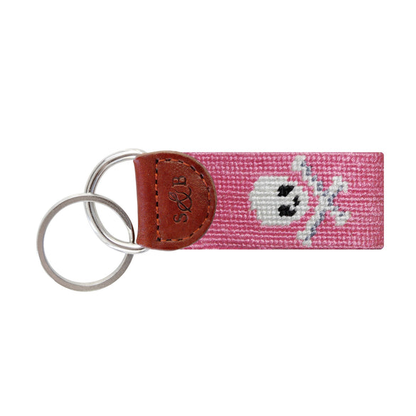 Pink needlepoint key fob with a white skull and crossbones (Jolly Roger), brown leather trim, and a metal key ring.