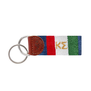 Green needlepoint key fob displaying the Greek letters ΚΣ in white, brown leather trim, and a metal key ring.