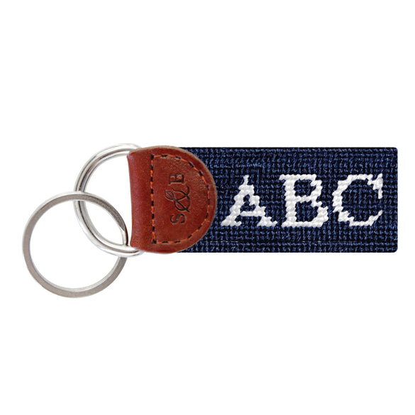 Dark navy needlepoint key fob featuring white monogram initials, brown leather trim, and a metal key ring.