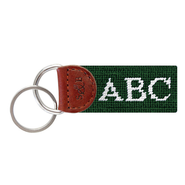 Hunter green needlepoint key fob featuring white monogram initials, brown leather trim, and a metal key ring.