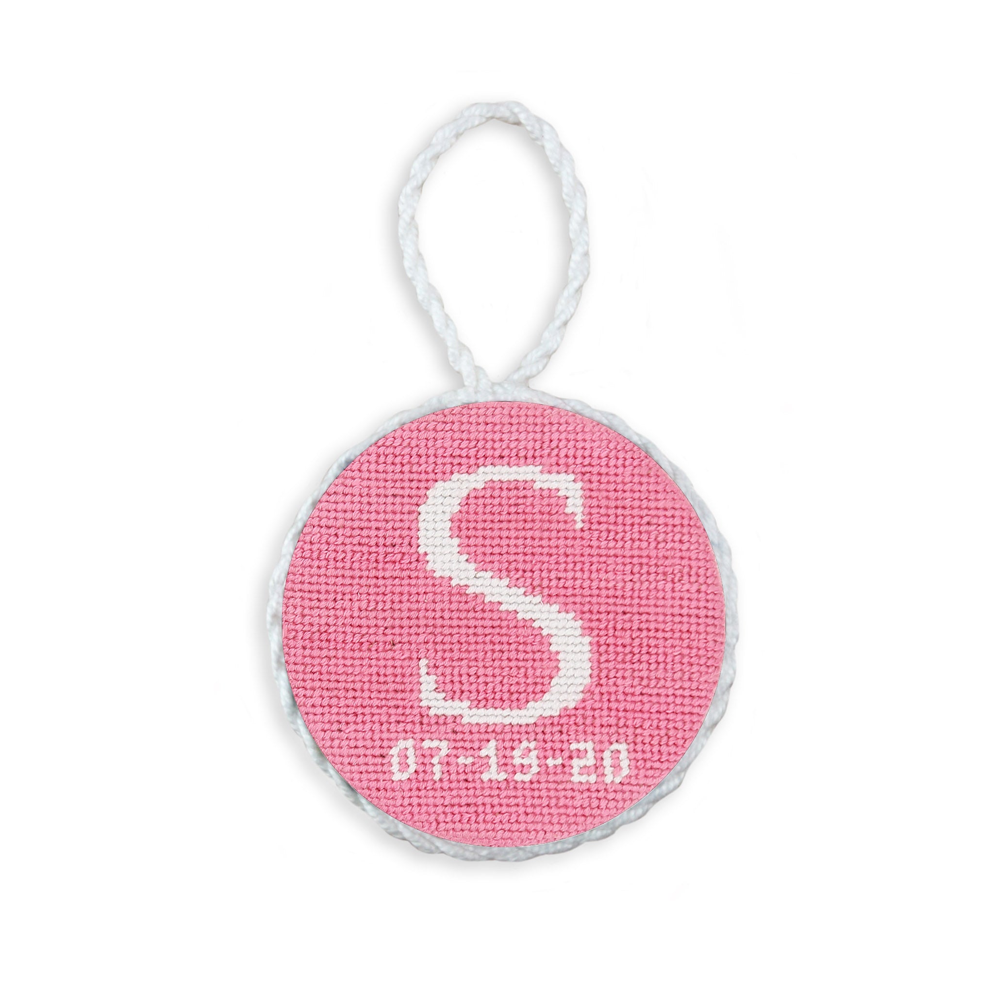 Pink needlepoint ornament with a scripted letter and date, white hanging cord.