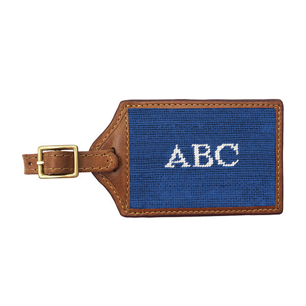 Black needlepoint luggage tag featuring white Block 10 monogram initials, brown leather trim, and an ID window on the back.