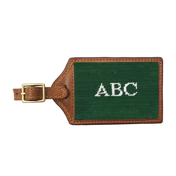 Garnet red needlepoint luggage tag featuring white Block 10 monogram initials, brown leather trim, and an ID window on the back.