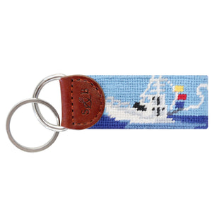 Blue needlepoint key fob showing an offshore fishing boat scene, brown leather trim, and a metal key ring.