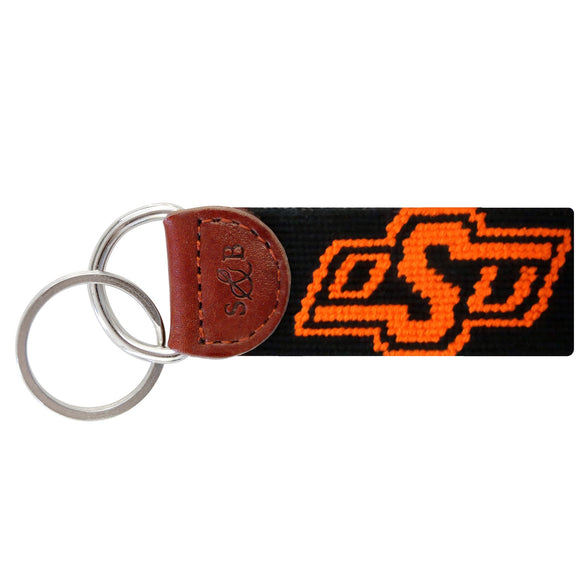 Black needlepoint key fob with the orange Oklahoma State “OSU” logo, brown leather trim, and a metal key ring.
