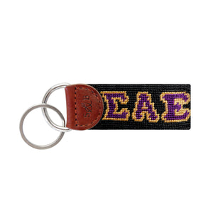 Navy needlepoint key fob featuring the Greek letters ΣΑΕ in gold, brown leather trim, and a metal key ring.