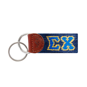 Royal blue needlepoint key fob displaying the Greek letters ΣΧ in white, brown leather trim, and a metal key ring.