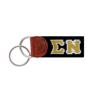 Black needlepoint key fob with the Greek letters ΣΝ in white, brown leather trim, and a metal key ring.