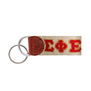 Navy needlepoint key fob featuring the Greek letters ΣΦΕ in red and gold, brown leather trim, and a metal key ring.