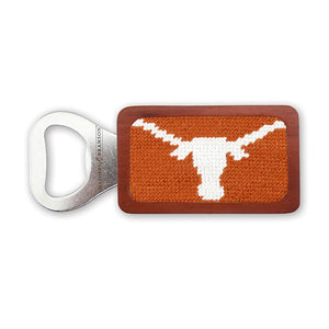 A stainless steel bottle opener with a wooden frame featuring a burnt orange needlepoint design embroidered with the white Texas "Long Horn" logo