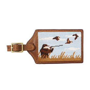 Olive green needlepoint luggage tag with an upland bird hunting scene, brown leather trim, and an ID window on the back.