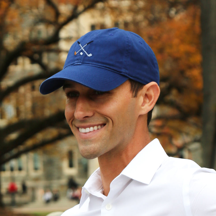 Man wearing a navy baseball cap featuring a golf club motif with a fall scenic backdrop