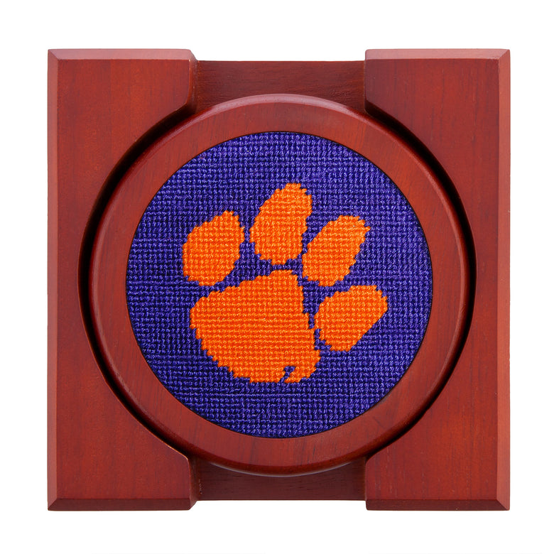 Orange needlepoint coaster displaying a white Clemson paw on one and coordinating designs on the rest, with chestnut wood backing.