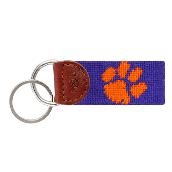 Purple needlepoint key fob with the white Clemson paw logo, brown leather trim, and a metal key ring.