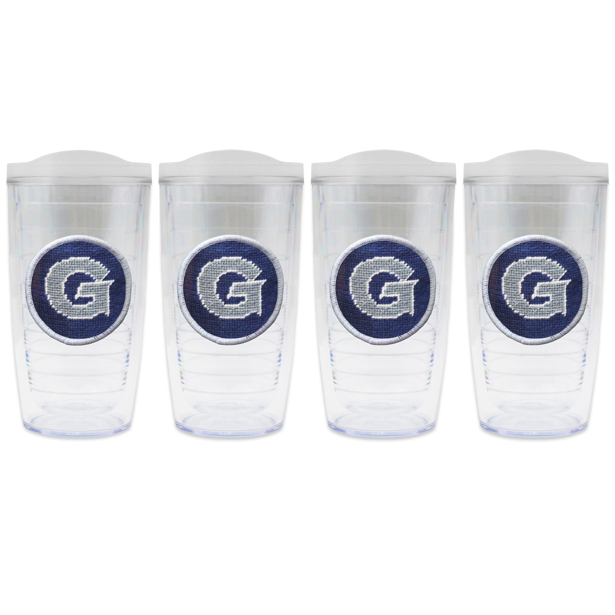 Set of 4 tumblers with lids on each in a line with a needlepoint logo in the center of each tumbler