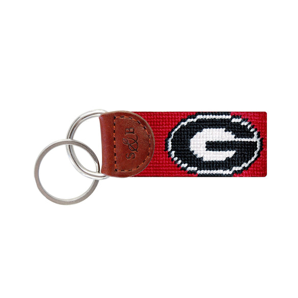 Red needlepoint key fob with a black Georgia “G” logo, brown leather trim, and a metal key ring.
