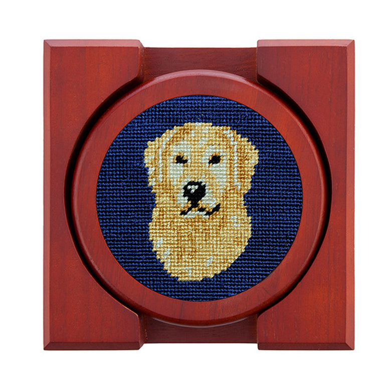 Set of four round wooden coasters with stitched needlepoint logos stacked neatly in a wooden holder.