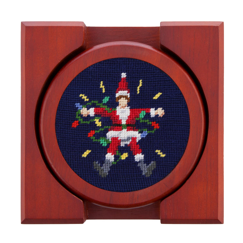 Set of four round wooden coasters with stitched needlepoint logos stacked neatly in a wooden holder.