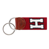 Garnet needlepoint key fob featuring the white Harvard “H” logo, brown leather trim, and a metal key ring.