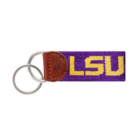 Purple needlepoint key fob with the LSU block letters in gold, brown leather trim, and a metal key ring.