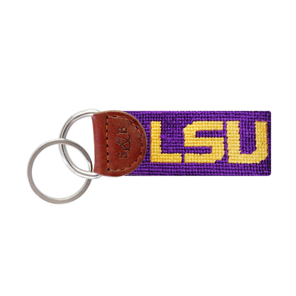 Purple needlepoint key fob with the LSU block letters in gold, brown leather trim, and a metal key ring.