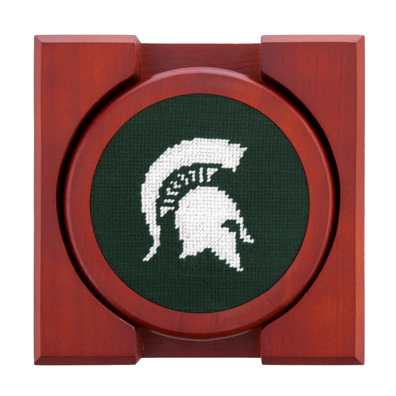 Set of four round wooden coasters with stitched needlepoint logos stacked neatly in a wooden holder.