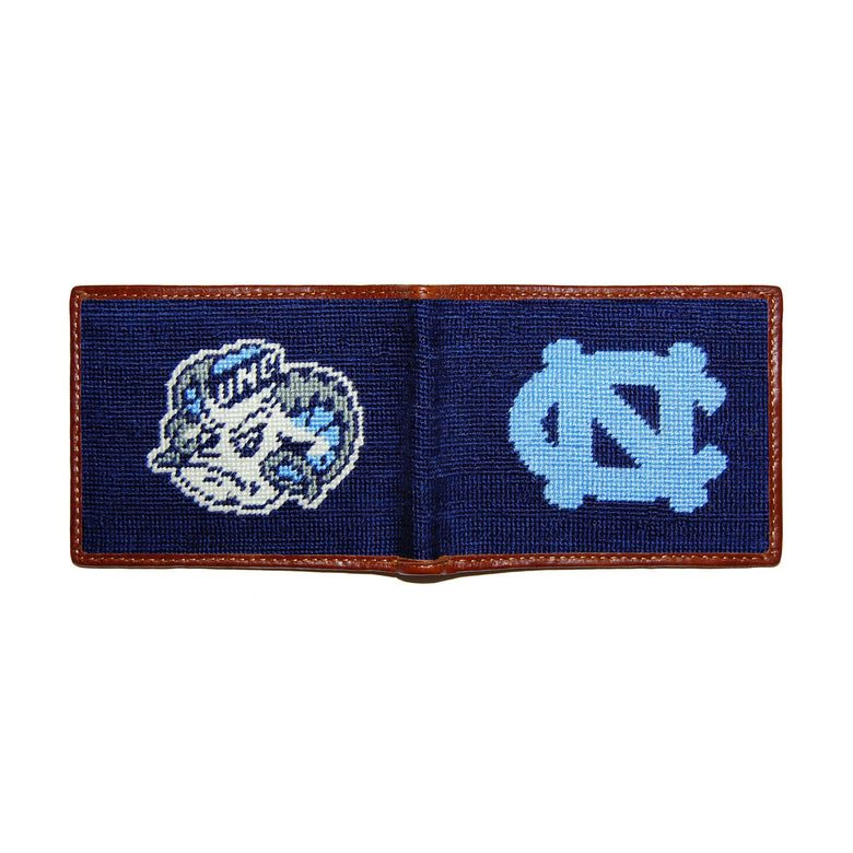 North Carolina navy needlepoint bi-fold wallet open to show both sides of the white “NC” interlocking logo needlepoint design with brown leather trim.