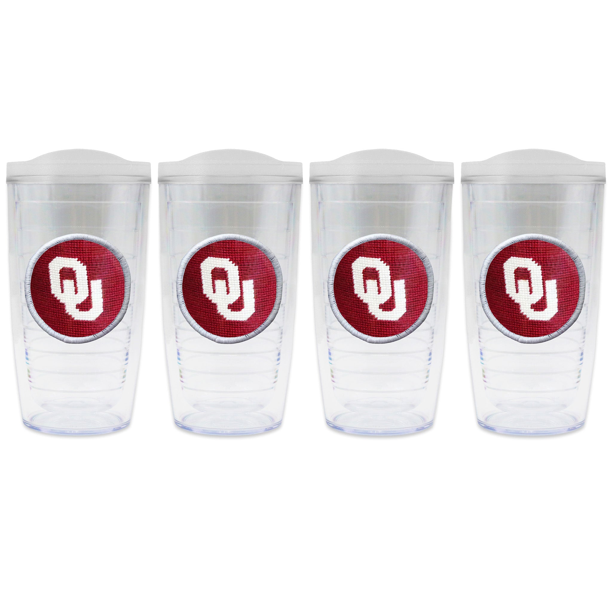 Set of 4 tumblers with lids on each in a line with a needlepoint logo in the center of each tumbler