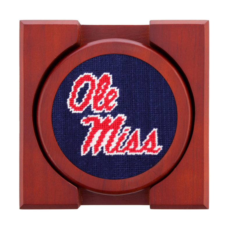 Navy needlepoint coasters with the “Ole Miss” script on one and complementary navy-red patterns, backed with chestnut wood.