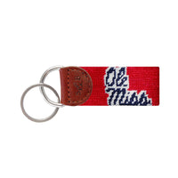 Red needlepoint key fob with gold Chi Omega Greek letters, brown leather trim, and a metal key ring.