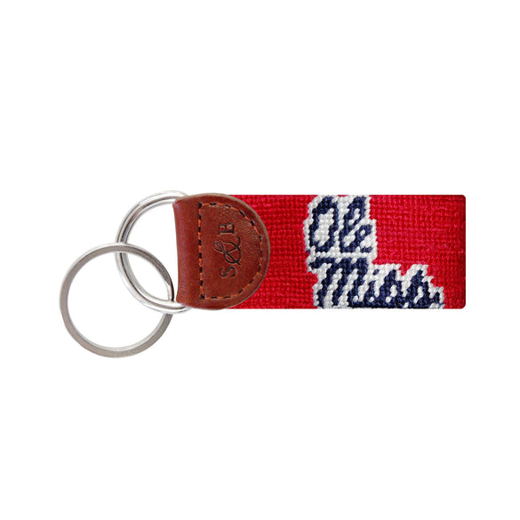 Red needlepoint key fob with gold Chi Omega Greek letters, brown leather trim, and a metal key ring.