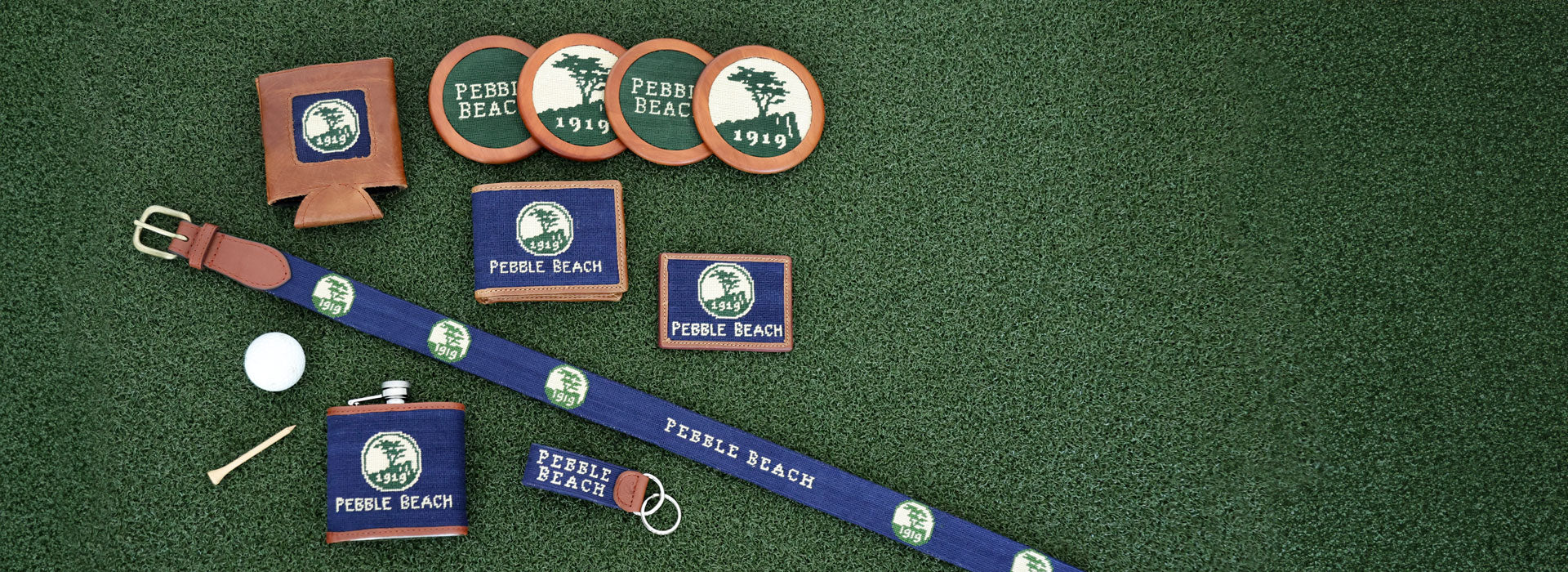 Collection of Pebble Beach-themed merchandise including a belt, flask, and can coolers on a green background.