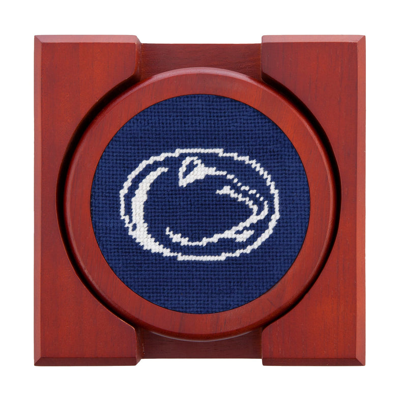 Set of four round wooden coasters with stitched needlepoint logos stacked neatly in a wooden holder.