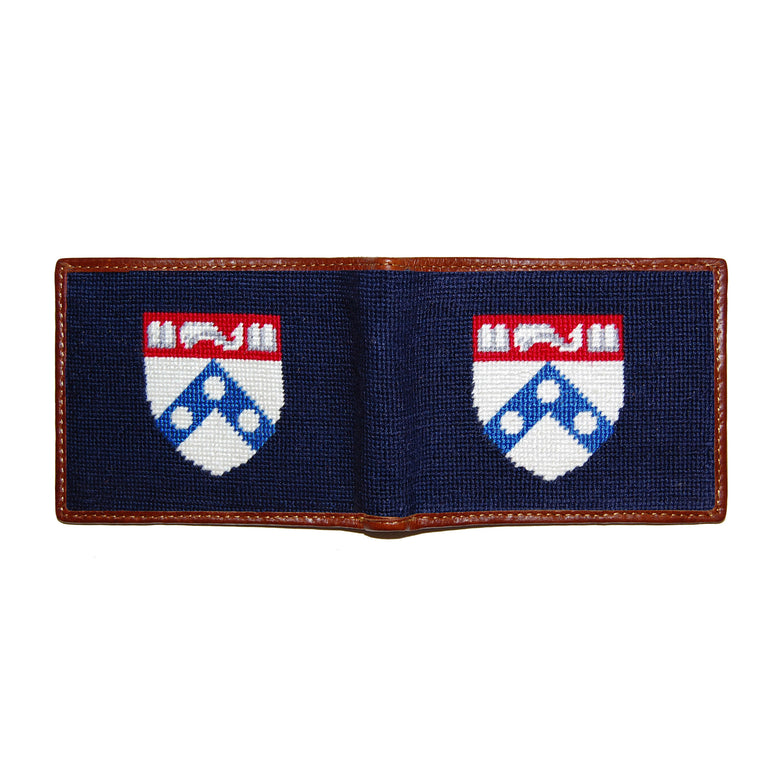 Pennsylvania navy needlepoint bi-fold wallet open to show both sides of the white “PENN” text needlepoint design with brown leather trim.