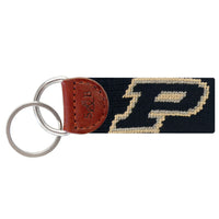 Black needlepoint key fob featuring the gold Purdue “P” logo, brown leather trim, and a metal key ring.