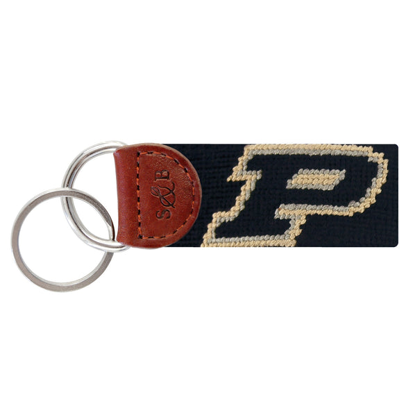 Black needlepoint key fob featuring the gold Purdue “P” logo, brown leather trim, and a metal key ring.